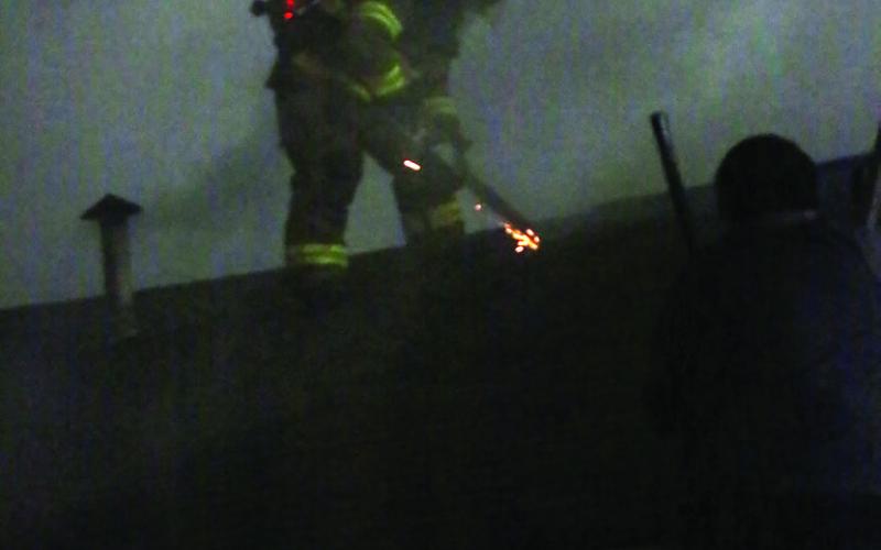 Cushing Firefighter Manuel Barron uses a chainsaw to ventilate the roof of a burning home on the 700 block of Broadway last week. Photo by J. D. Meisner