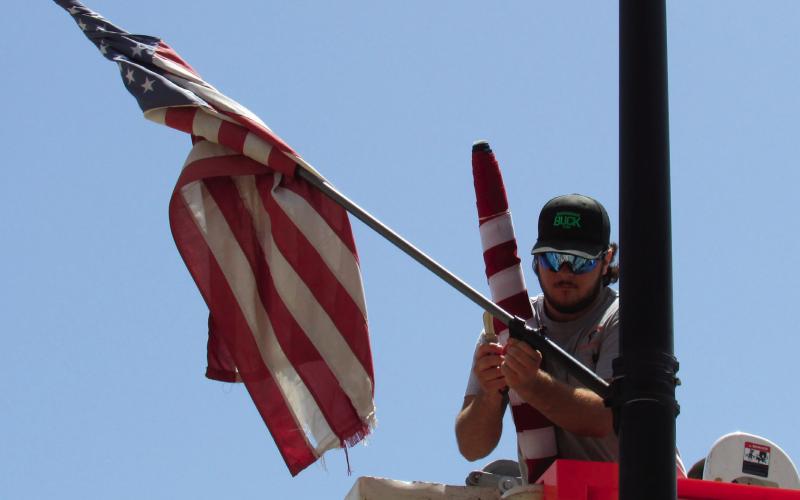 Apprentice lineman with the Electric Distribution department, Tagun Fittje, was replacing damaged flags in the Broadway District last week prior to the holiday festivities. As part of flag etiquette whenever a flag is worn or damaged beyond repair the flag should be destroyed by burning it.