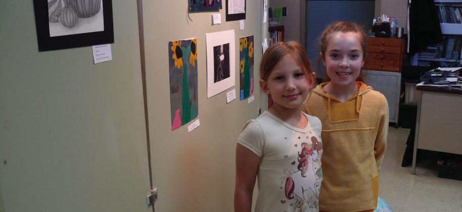Eden Goodman and Hailey Wittman pose in front of a wall of art at the Lachenmeyer Arts Center Youth Art Show.