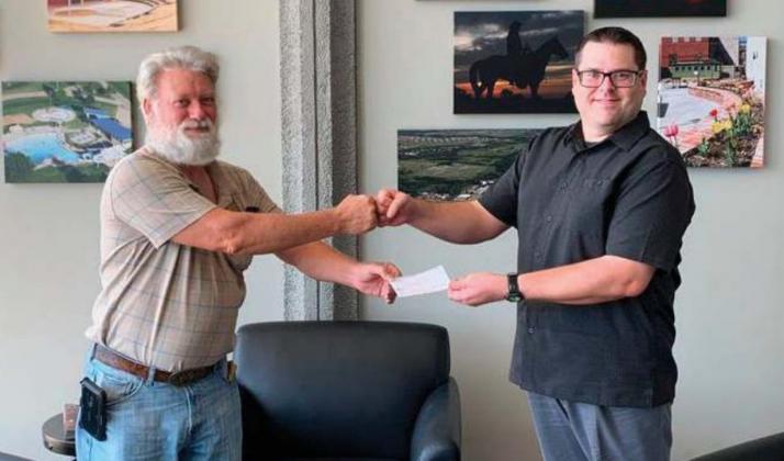 Charles Whittom, left, and Michael Hanes fi st bump as Whittom accepts a $900 donation from the Cushing Genealogical Society to support repairs to the Library’s microfi che machine.