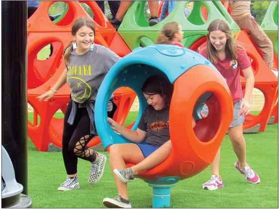 Fifth grade student Brooklyn Pierce takes a spin as classmates Tegan Sherman and Melanee Robnett propel her in one of the new pieces of playground equipment at Cushing Middle School.