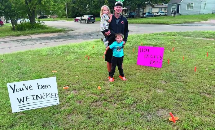 Assistant cross country coach Mason Baade and his sons Eamon and Beckett survey the wurst landscaping job ever after Cushing’s high school girls cross country team planted hot dogs and buns on skewers in his yard. Signs reading “You smell like buns” “You’ve been weinered” and “Hot diggity dog” identified the prank, but the perpetrators were already on the run. See page 6 &amp; 7 for CHS cross country state qualifiers. Photo by Keaghan Baade.