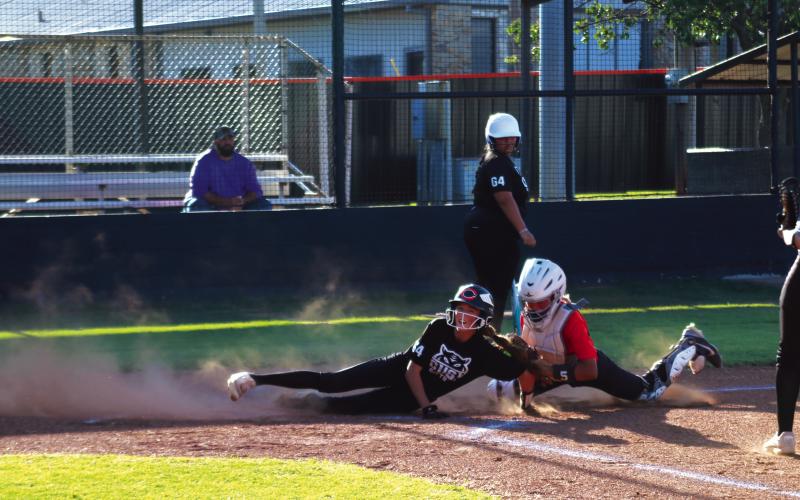 Harli York slides safe at home while Talyn Minney attempts the tag during the Black and Orange fast pitch scrimmage Thursday. Raina Foster spectates from the background. Photo by J. D. Meisner