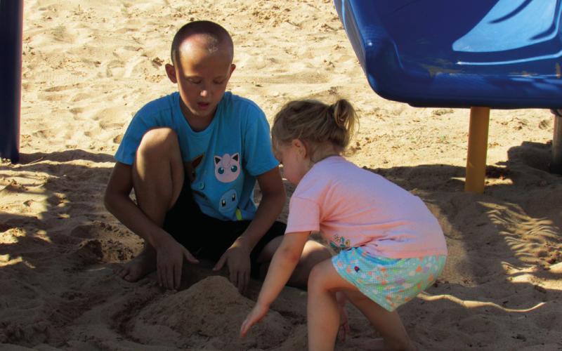 Siblings Luke Bush and Sophie Hoover work on a sandcastle, shaded by playground equipment, in Memorial Park during a recent sunny summer day.