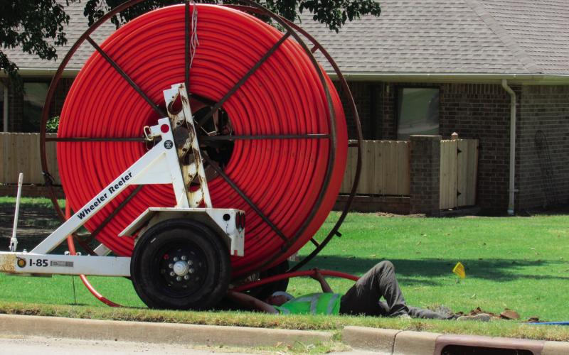 A utility worker threads bright orange fiber optic cable into underground conduit along Linwood street out by Sinclair as part of a broadband infrastructure project.