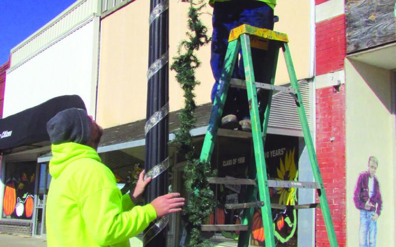 Cushing Parks Department member Marty Rylant stands atop a ladder straightening greenery as Eric Sams waits below to twirl the decoration around a light post on Broadway Street on Tuesday, Nov. 15 in preparation of the upcoming holidays. Photo by DeAnna Maddox.