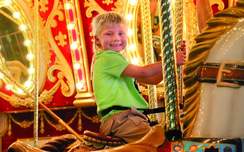 Hutson Boos, of Cushing, celebrates his fifth birthday by smiling upon his kingdom (The Payne County Free Fair) atop his noble steed (while riding the carousel) Thursday, Aug. 29. Photo by Allie Prater