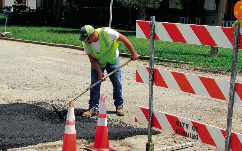 Dakota Hatfield evens out asphalt at the corner of East Avenue and 2nd Street on July 16. A section of road had to be removed previously to repair a waterline in the area. The process to fix the road can be both costly and lengthy, according to Hatfield, due to material cost being expensive and the street crew consisting of only four people for the entire city of Cushing.
