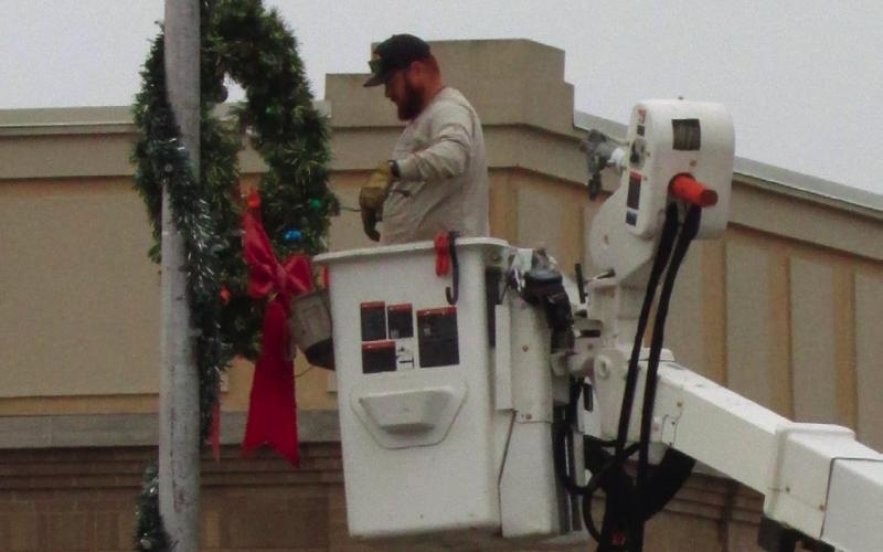 Brendan Campbell spreads Christmas cheer as he hangs a wreath on a light post at Harrison and Moses. Photo by DeAnna Maddox