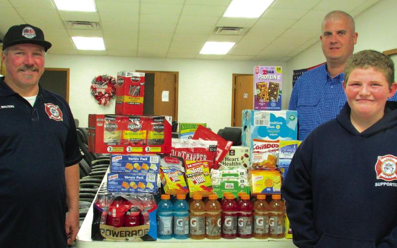 Firefighters Casey Walters and Kyle Wolff stand with Owen Seitsinger after he made a generous donation of drinks, snacks, and baby wipes to the Agra Volunteer Fire Department.