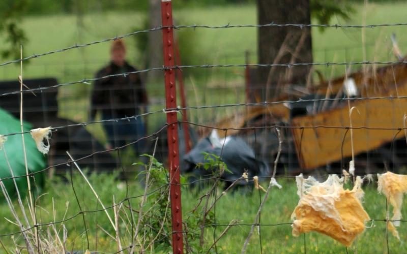 Bits of fiberglass insulation clings to a barbed wire fence as Kimberly Willson surveys the damage to her livestock pens Tuesday morning. Photo by J. D. Meisner