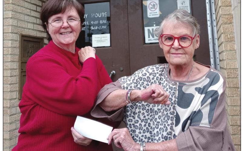 Marsha Grace presents a check to Carol Arwen, Friends of the Library president and Library Director, Michael Hanes on the steps of the Cushing Public Library.