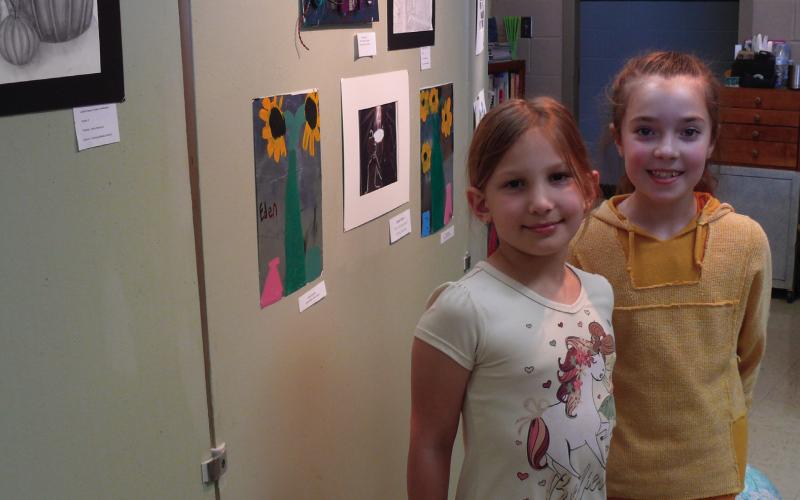Eden Goodman and Hailey Wittman pose in front of a wall of art at the Lachenmeyer Arts Center Youth Art Show.
