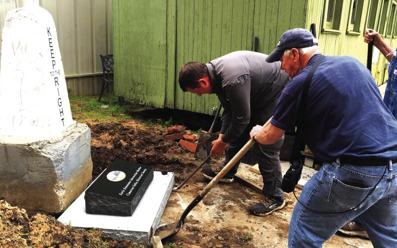 Cimarron Valley Historical Society President Farrel Kleckner, foreground, and Zach Howser, owner of Williams Monuments square up the commemorative stone in front of the recently placed intersection marker at Centennial Park.