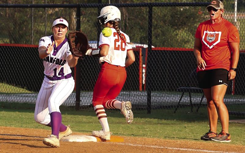 Cushing Lady Tiger junior Romy Withiam makes it to first base seconds before Mannford Lady Pirate first baseman Sydney Webster catches the ball as Lady Tiger head coach Nikki York watches from the coach’s box during the Lady Tigers game Tuesday, Aug 22. Photo by Allie Prater