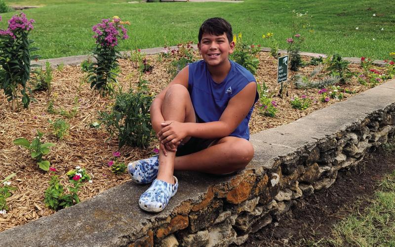 Jaxon Bell sits proudly at the edge of his finished project — he gave special thanks for its completion to Kaden Ledgerwood with Ironside Enterprises, Derek Bell with Proverbs Landscape, Hilltop Greenhouse, community volunteers, and GoFundMe donors.