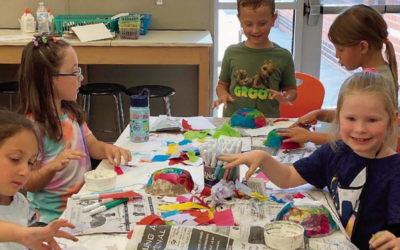 Younger art students embellishing paper mache masks during the 31st Summer Art Camp that was recently completed.