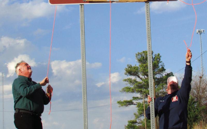 Jim McFarlin and Jarrod Molloy pull back on rope to reveal the Dale McFarlin Memorial Highway sign displayed on State Highway 18 just before entering Agra.