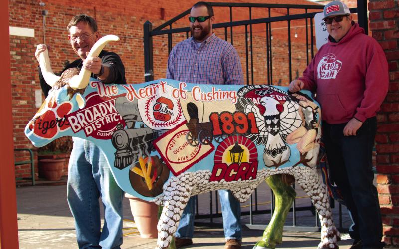 John Moran, Tyler Stein and Justin Cargill show off the Downtown Cushing Revitalization Association’s longhorn steer which they installed at Centennial Park in Cushing last Friday. The artwork on the steer, painted by Stein, depicts historical highlights from Cushing’s past on one side and highlights from the oil industry on the other. Photo by J. D. Meisner