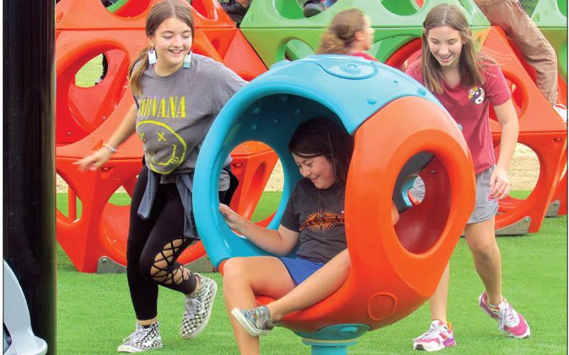 Fifth grade student Brooklyn Pierce takes a spin as classmates Tegan Sherman and Melanee Robnett propel her in one of the new pieces of playground equipment at Cushing Middle School.