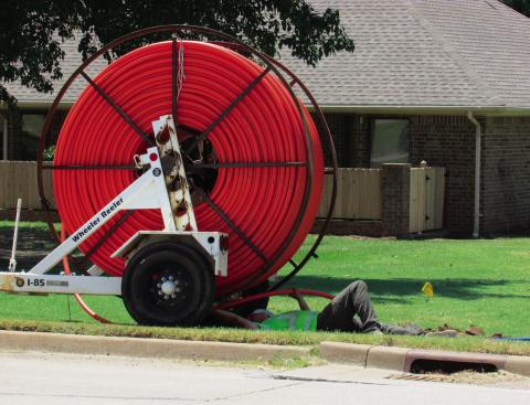 A utility worker threads bright orange fiber optic cable into underground conduit along Linwood street out by Sinclair as part of a broadband infrastructure project.