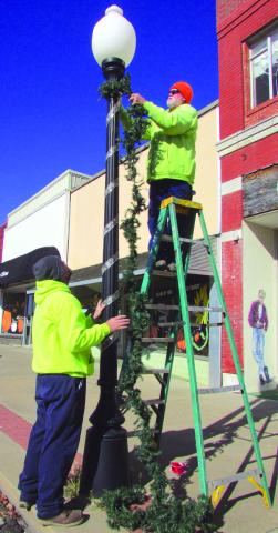 Cushing Parks Department member Marty Rylant stands atop a ladder straightening greenery as Eric Sams waits below to twirl the decoration around a light post on Broadway Street on Tuesday, Nov. 15 in preparation of the upcoming holidays. Photo by DeAnna Maddox.