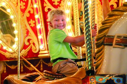 Hutson Boos, of Cushing, celebrates his fifth birthday by smiling upon his kingdom (The Payne County Free Fair) atop his noble steed (while riding the carousel) Thursday, Aug. 29. Photo by Allie Prater
