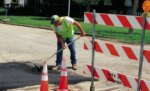 Dakota Hatfield evens out asphalt at the corner of East Avenue and 2nd Street on July 16. A section of road had to be removed previously to repair a waterline in the area. The process to fix the road can be both costly and lengthy, according to Hatfield, due to material cost being expensive and the street crew consisting of only four people for the entire city of Cushing.