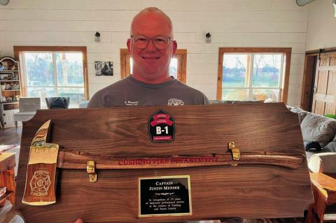 Newly retired Cushing Fire Department Captain Justin Menser displays a golden axe given to him to commemorate 25 years of service.