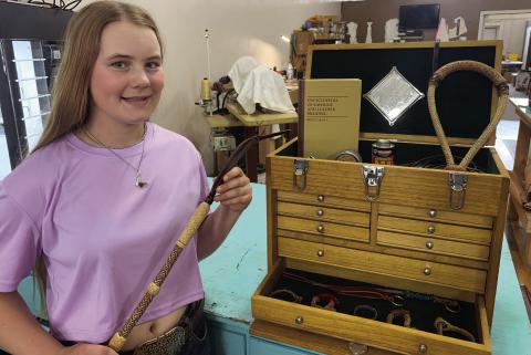 Mercedes Cargill with her rawhide braiding box, filled with tools and items she’s braided, such as a bosal (top right), bracelets (bottom) and quirt (in hand).