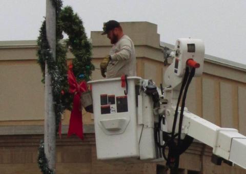 Brendan Campbell spreads Christmas cheer as he hangs a wreath on a light post at Harrison and Moses. Photo by DeAnna Maddox