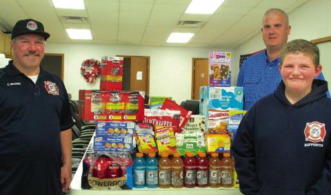Firefighters Casey Walters and Kyle Wolff stand with Owen Seitsinger after he made a generous donation of drinks, snacks, and baby wipes to the Agra Volunteer Fire Department.