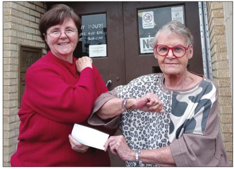 Marsha Grace presents a check to Carol Arwen, Friends of the Library president and Library Director, Michael Hanes on the steps of the Cushing Public Library.
