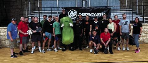 Tournament participants pose with Big Dill the mascot for Pickleman’s Gourmet Cafe, in Stillwater after the Mercury Marine Fourth Annual Pickleball Tournament.
