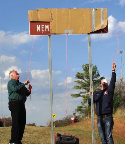 Jim McFarlin and Jarrod Molloy pull back on rope to reveal the Dale McFarlin Memorial Highway sign displayed on State Highway 18 just before entering Agra.