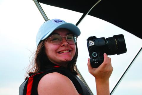 Raynee Howell smiling, camera in hand, while doing an ‘on the job’ interview with an USACE ranger on the lake patrol boat at Keystone Lake in May. Photo by Allie Prater