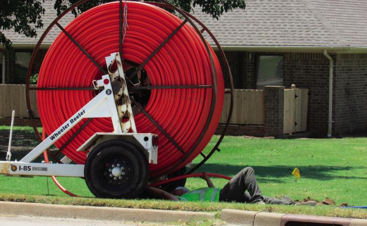 A utility worker threads bright orange fiber optic cable into underground conduit along Linwood street out by Sinclair as part of a broadband infrastructure project.