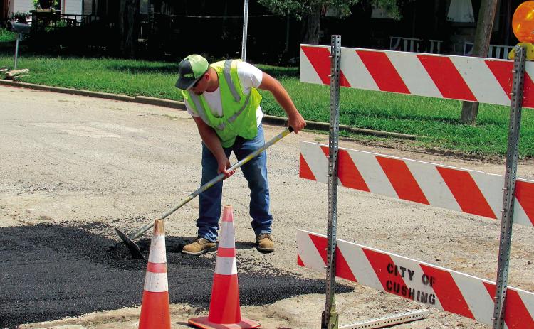 Dakota Hatfield evens out asphalt at the corner of East Avenue and 2nd Street on July 16. A section of road had to be removed previously to repair a waterline in the area. The process to fix the road can be both costly and lengthy, according to Hatfield, due to material cost being expensive and the street crew consisting of only four people for the entire city of Cushing.
