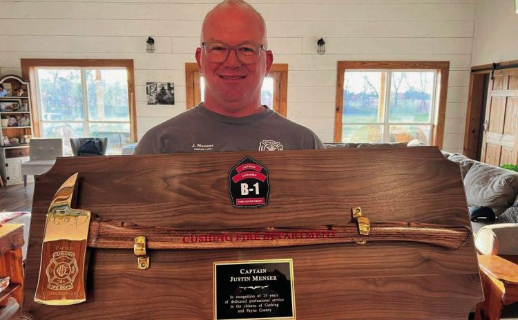 Newly retired Cushing Fire Department Captain Justin Menser displays a golden axe given to him to commemorate 25 years of service.