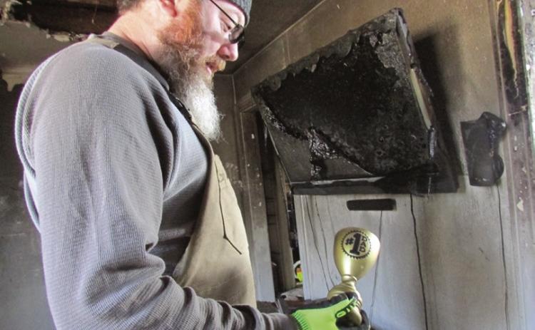Jeremy Fincher holds a “worlds best dad” trophy while standing in the ruins of his family’s home.