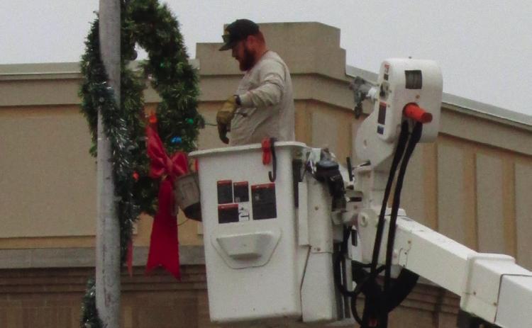 Brendan Campbell spreads Christmas cheer as he hangs a wreath on a light post at Harrison and Moses. Photo by DeAnna Maddox