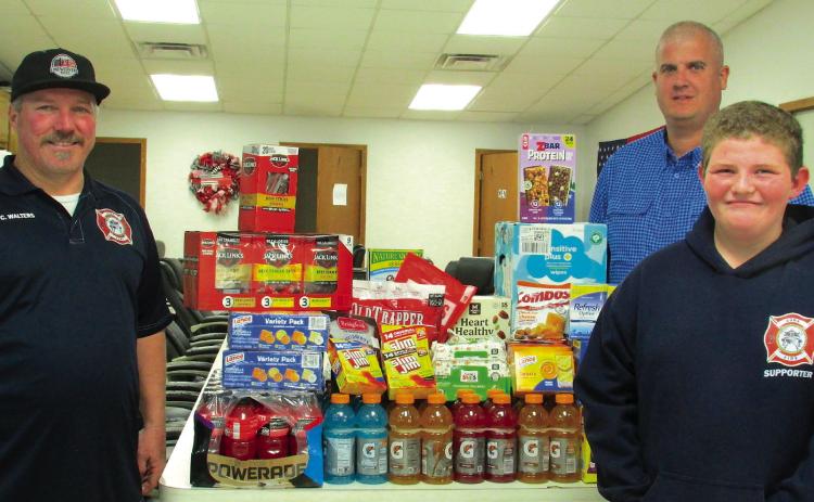 Firefighters Casey Walters and Kyle Wolff stand with Owen Seitsinger after he made a generous donation of drinks, snacks, and baby wipes to the Agra Volunteer Fire Department.