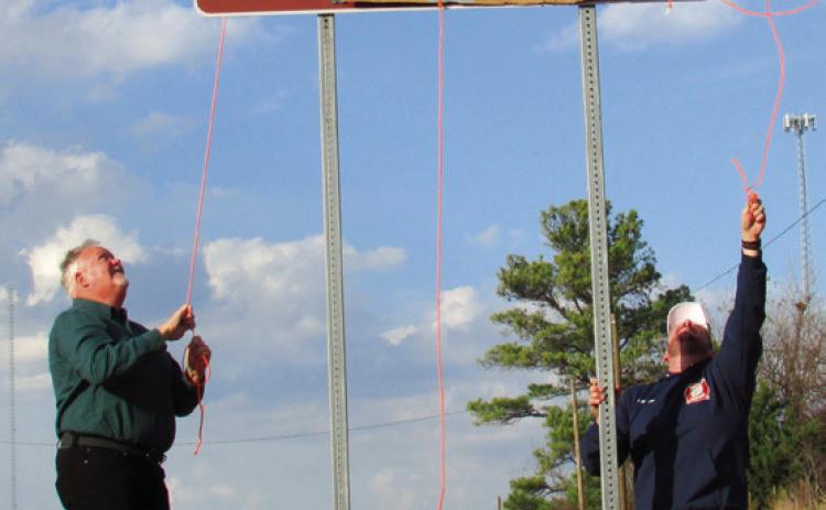 Jim McFarlin and Jarrod Molloy pull back on rope to reveal the Dale McFarlin Memorial Highway sign displayed on State Highway 18 just before entering Agra.