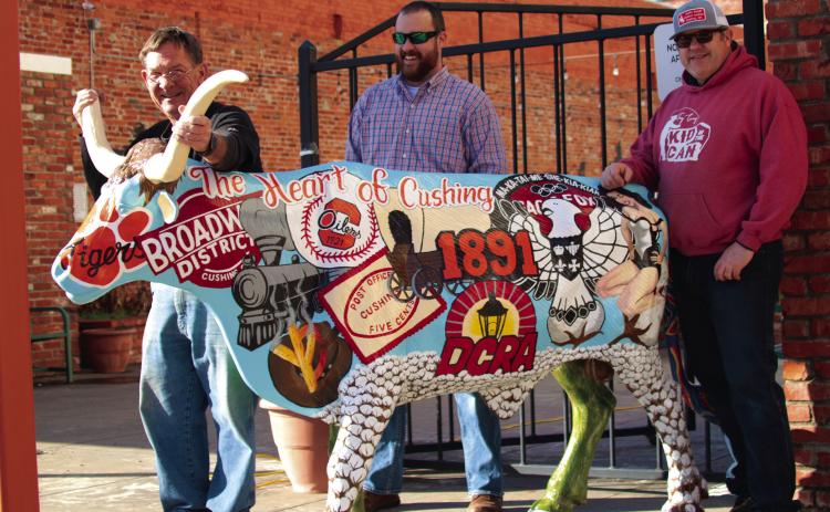 John Moran, Tyler Stein and Justin Cargill show off the Downtown Cushing Revitalization Association’s longhorn steer which they installed at Centennial Park in Cushing last Friday. The artwork on the steer, painted by Stein, depicts historical highlights from Cushing’s past on one side and highlights from the oil industry on the other. Photo by J. D. Meisner