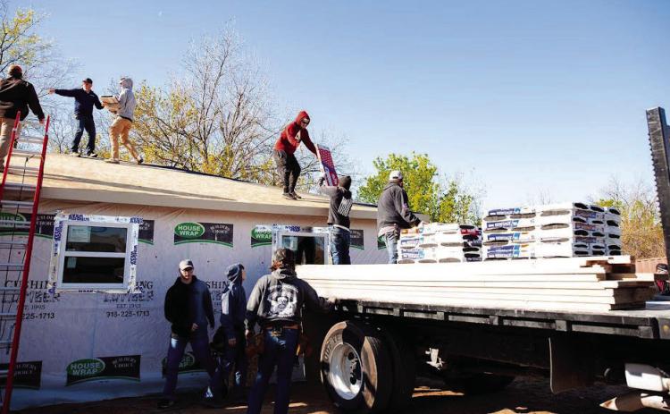 Construction students at Central Tech load shingles on the roof of the house they are building.
