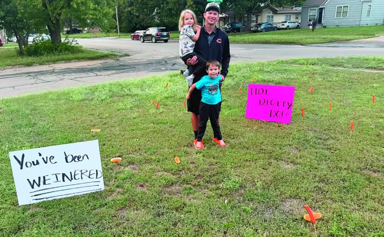 Assistant cross country coach Mason Baade and his sons Eamon and Beckett survey the wurst landscaping job ever after Cushing’s high school girls cross country team planted hot dogs and buns on skewers in his yard. Signs reading “You smell like buns” “You’ve been weinered” and “Hot diggity dog” identified the prank, but the perpetrators were already on the run. See page 6 &amp; 7 for CHS cross country state qualifiers. Photo by Keaghan Baade.